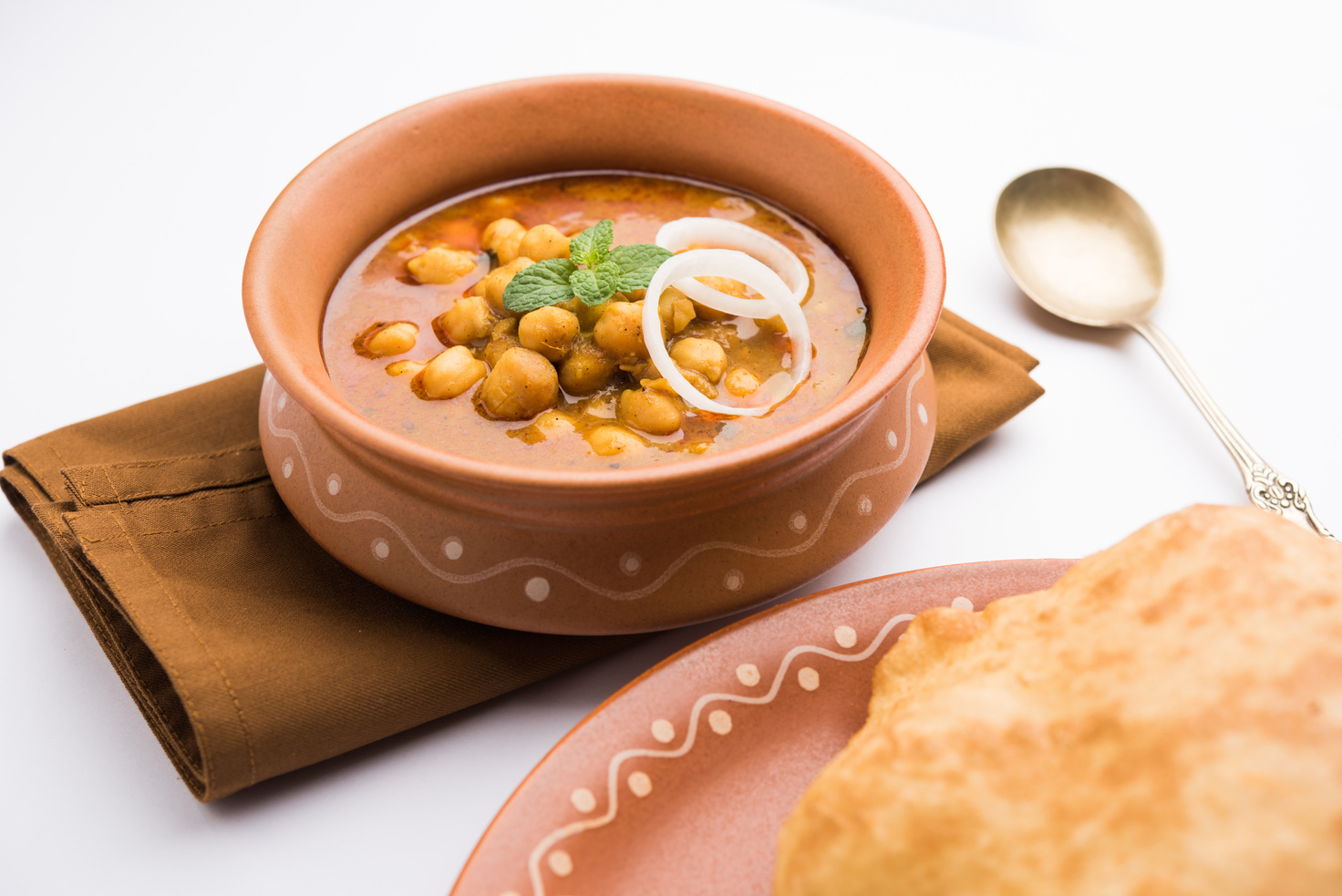 Chole Bhature or Chick pea curry and Fried  Puri served in terracotta crockery over white background. selective focus